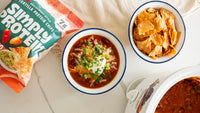 Two bowls of chili with tortilla chips next to a package of Simply Protein tortilla chips.