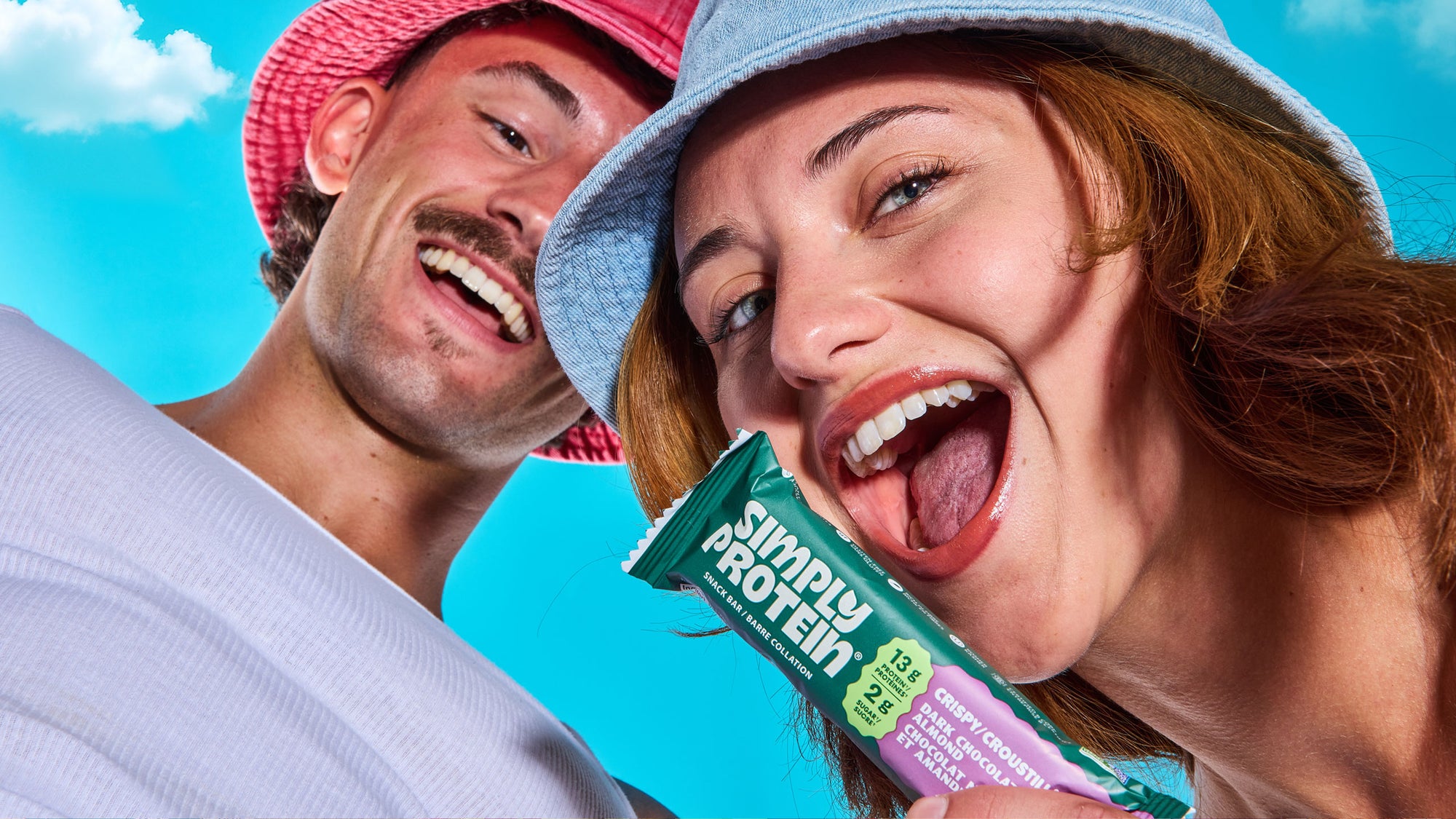 Two people holding a Simply Protein bar against a blue sky background