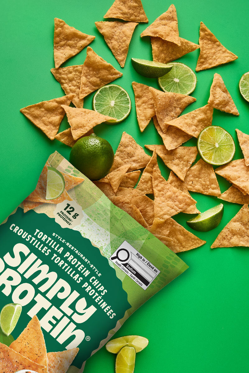 Simply Protein tortilla chips with lime wedges on a green background
